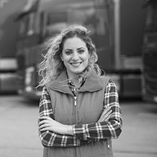 woman in vest and flannel standing in front of semi trucks